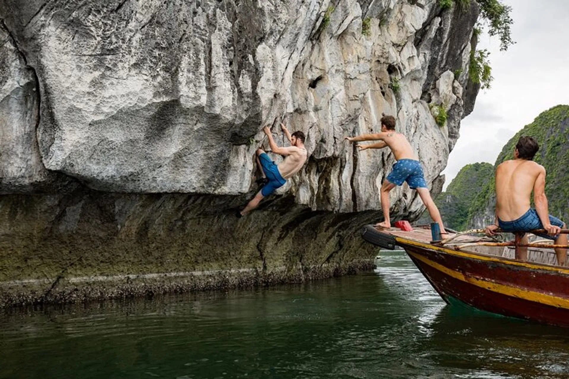 A climber on a limestone wall above the water beside a support boat