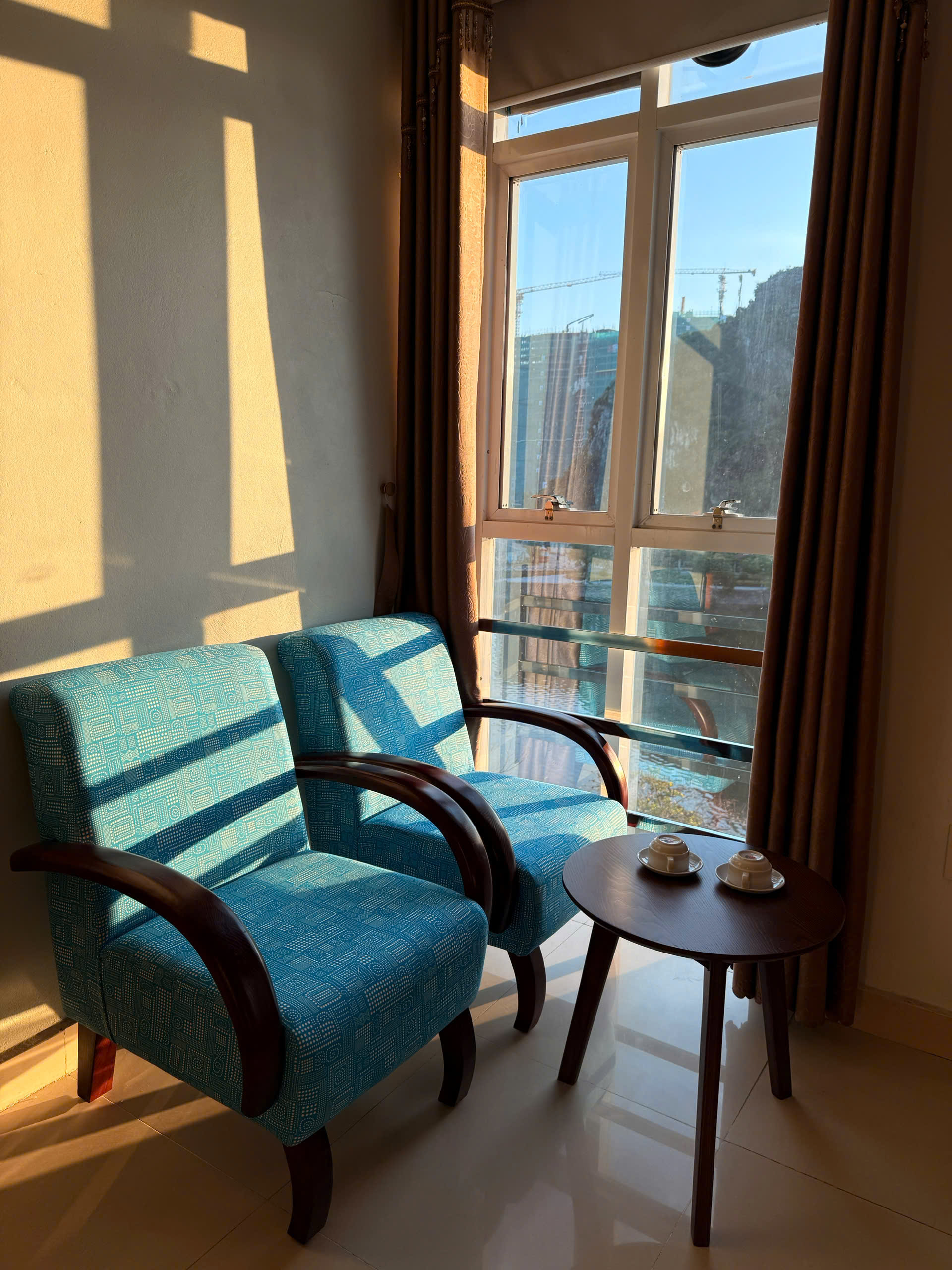 Two blue armchairs and a tea table beside a sunny hotel-room window
