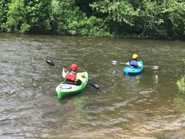 Two kayakers wearing long-sleeved layers and flotation vests on a river