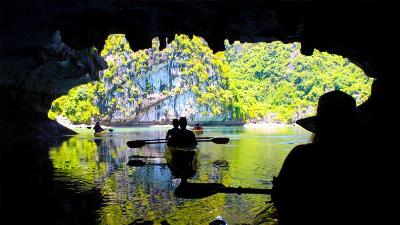 Kayakers seen from inside a water cave looking out onto a green lagoon