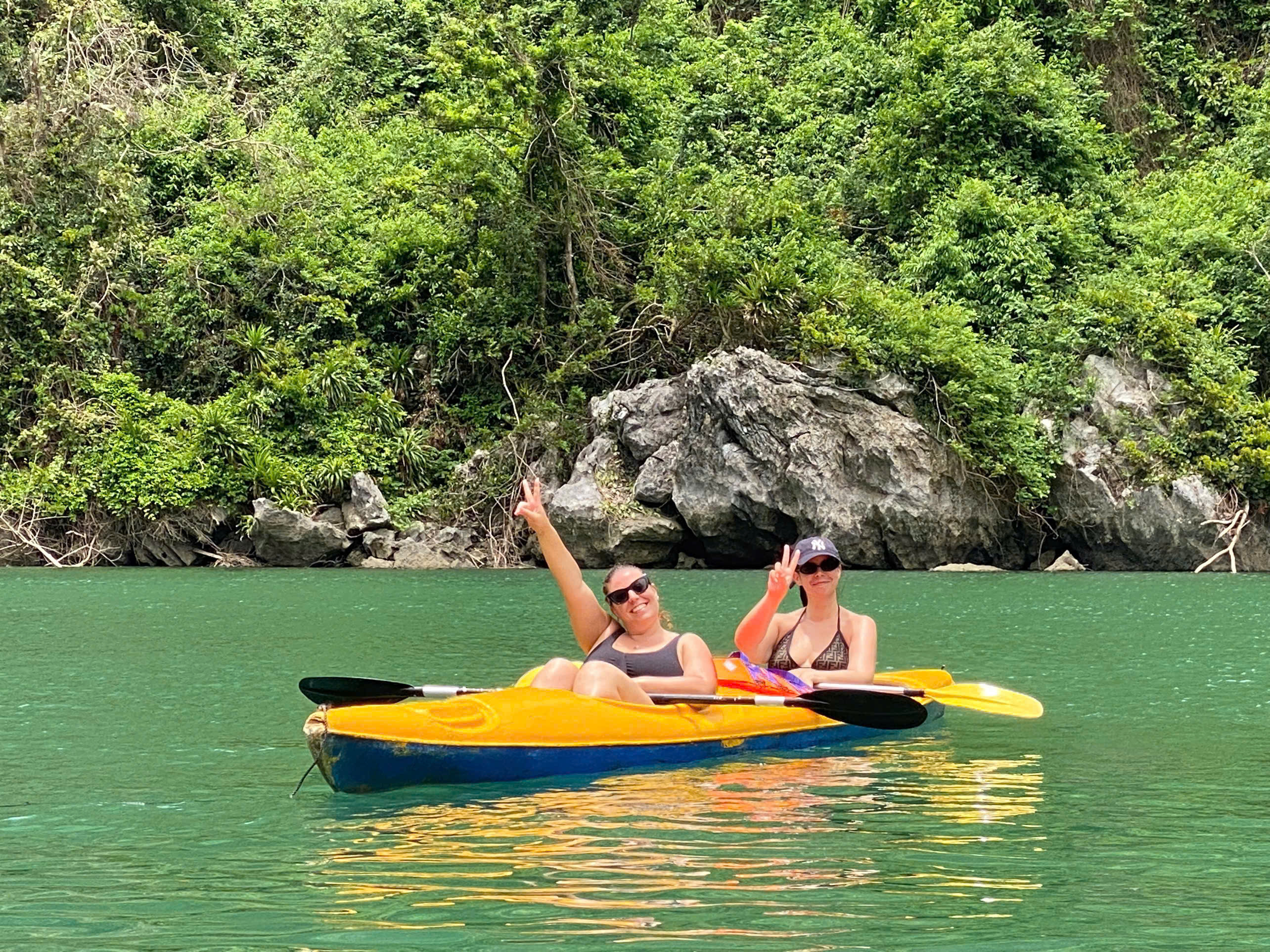 Guests in a yellow kayak beside limestone cliffs in Lan Ha Bay
