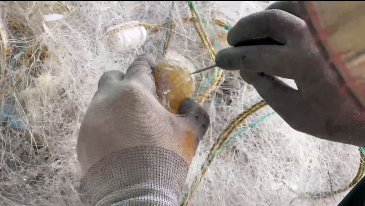 Hands untangling a fishing net at a floating home