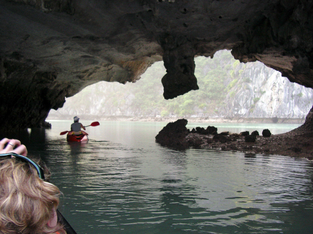 Kayaker passing beneath a low limestone cave near Cat Ba