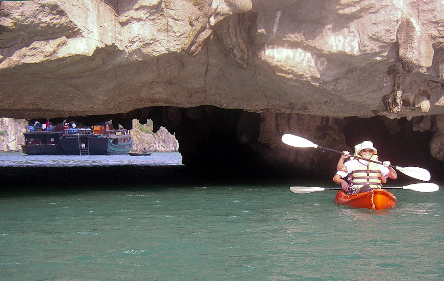 Kayakers inside a Ha Long Bay lagoon looking toward its low cave opening